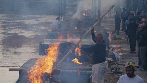 Pashupatinath, Kathmandu, Nepal. 12-15-2019. Bodies being cremated at Pashupatinath temple ghats and man moving a body so it can burn properly.