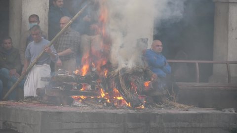 Pashupatinath, Kathmandu, Nepal. 12-15-2019. Close up of body burning at Pashupatinath temple ghats while family watch in the backgroung.