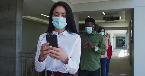 Multi-ethnic group working in casual office, in face mask protecting from Covid 19 standing in line using smartphones slow motion. Social distancing in workplace during Coronavirus Covid 19 pandemic.