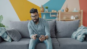 Portrait of joyful Arab guy playing vido game using joystick looking at camera at home enjoying modern device. Entertainment and technology concept.