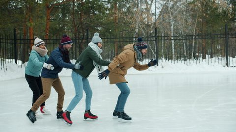 Slow motion of playful men and women having fun ice-skating and laughing in park on winter day. Youth lifestyle and outdoor activities concept.