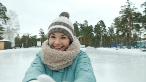 Portrait of happy young woman in warm clothes ice-skating laughing having fun looking at camera in park in winter. Recreational activities and youth concept.