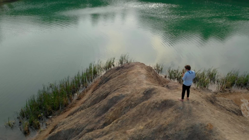 The musician plays the saxophone standing on the mountains and rocks near the reservoir. Aerial view from above on a warm summer day.