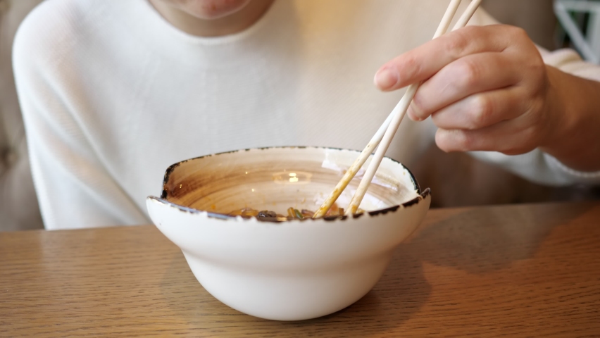 Young unrecognizable woman eating transparent noodles with seafood in a cafe.