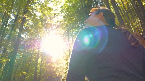SLOW MOTION, LENS FLARE, CLOSE UP: Girl enjoys a relaxing trek around a forest changing colors. Fit young woman hiking in Slovenia observes the beautiful autumn colored forest on a sunny fall day.