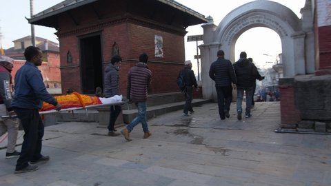 Pashupatinath, Kathmandu, Nepal. 12-15-2019. Side view of body being taken to be cremated and people looking at Pashupatinath temple ghats .