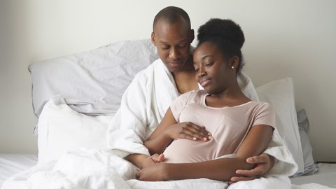 Young african black family, pregnant woman and man lie on bed in morning, at home.
