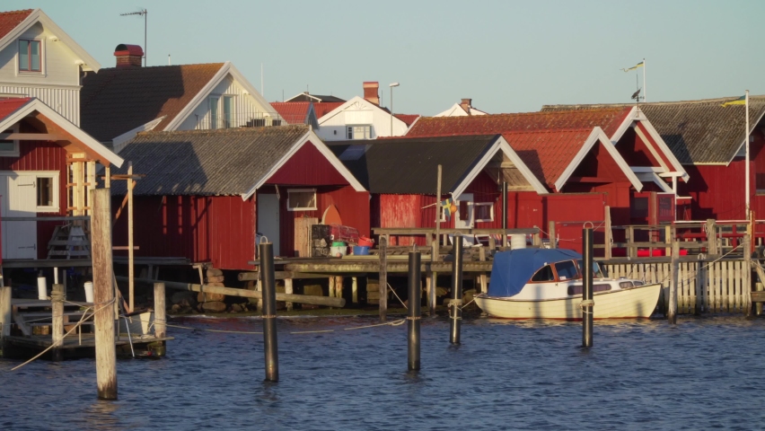 Sweden fishing cabin on west coast in bohuslan Orust island. Ocean dock and boats in sunset light. Red vacation homes by the sea. Smooth walking gimbal shot in 4k. Swedish flag traditional buildings