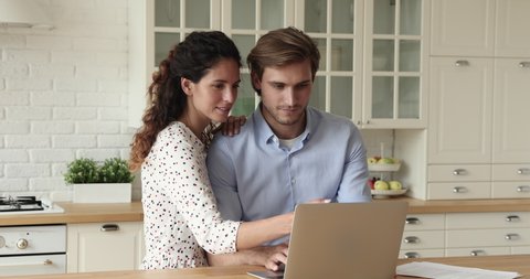 Couple 30s wife and husband in kitchen using laptop enjoy e-shopping remotely, planning future relocation choose renovation firm services online. E-commerce easy and comfort activity from home concept