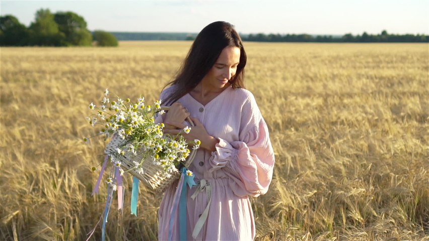 Beautful woman in wheat field in dress with a bouquet of chamomile in hands