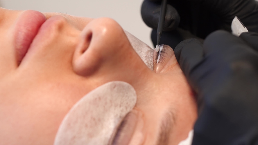 Closeup view 4k video of female face of young girl and professional cosmetologist doing modern spa cosmetic procedures of lashes lamination. | Shutterstock HD Video #1060021574