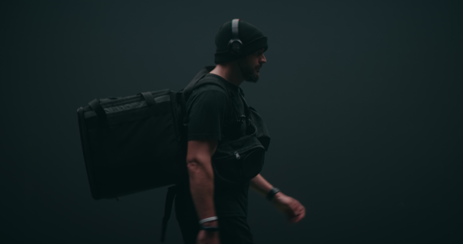 Caucasian male courier walking with a delivery backpack against black background. Shot on RED cinema camera