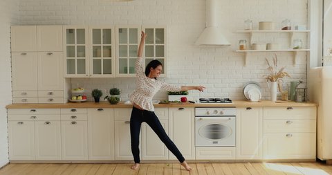 Wide full-length wide view in modern spacious kitchen lively housewife singing feels happy, dancing barefoot on warm floor with underfloor heating system. Hobby and luxury home owner free time concept