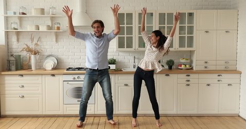 Full length couple dancing together in cozy spacious domestic kitchen while listen energetic music feels cheerful. Dating and relationships, happy home owners celebrate relocation at new house concept