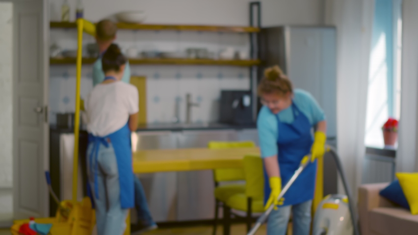 Professional cleaning team in uniform working in modern loft apartment. Portrait of smiling woman janitor with hands crossed posing at camera with colleagues cleaning on background | Shutterstock HD Video #1060026869