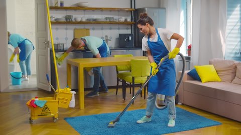 Professional team of janitors vacuum cleaning carpet, wiping furniture and washing bathroom. Home cleaning service crew working in modern loft apartment