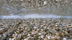 Pebbles rocks underwater below water surface with small waves breaking on the shore, Mediterranean sea, France