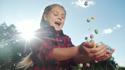 kid fun dream concept. little girl catches with her hands a large stream of multicolored sweets. kid in the park rejoices as candy is poured. dream of a small child in fun childhood