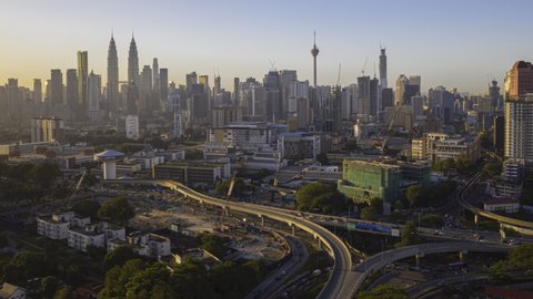 Malaysia Time lapse Sunrise : Aerial city at dawn overlooking Kuala Lumpur city skyline & Kuala Lumpur General Hospital with busy roundabout and streets. Pan up motion timelapse. Prores 4KUHD
