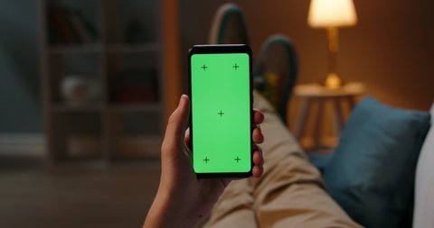 Man lying on couch using smartphone with chroma key green screen at night, scrolling through social media or online shop - internet, communications concept close up 4k template Stock Video