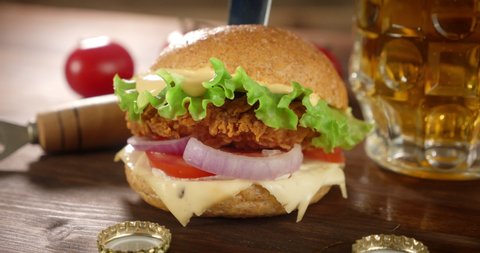 A burger with chicken fillet and a glass of beer rotate. On a wooden background.