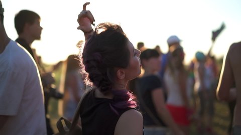 Music fans enjoying summer gig. Concept of youth culture and entertainment. Pretty asian woman dancing at sunset light among the crowd of people at rock concert festival.