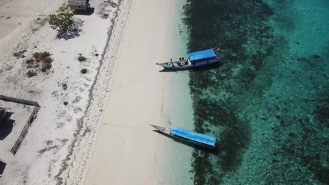 A drone shot of boats anchored to a beach on an island near Maumere, Indonesia. Clear, turquoise coloured water displaying coral reef. Deeper and darker see in the back. Fishing boat. Serenity
