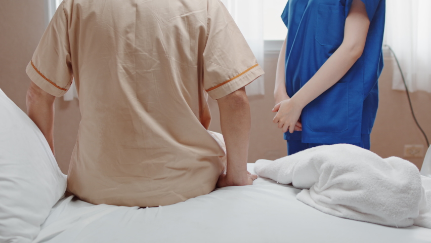 Female Asian nurse support senior male patient stand up and walk from bed in hospital. Nursing home, medical service, physiotherapy, hospitality, or recovery treatment concept Royalty-Free Stock Footage #1060044530