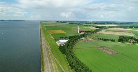 Aerial wide angle view of typical Dutch agricultural landscape along dike with green fields in the foreground blue sky with clouds casting shadows on the land. Wind turbines in the background, Holland