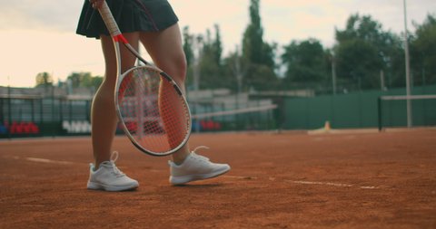 slow-motion side view of a young athlete trains the serve of the tennis ball. A teenage athlete is playing tennis on a court. An active girl is powerfully hitting a ball during sport practicing