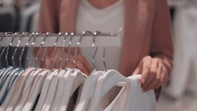 Close up with mid-section of unrecognizable young woman looking through clothes rack while shopping in store