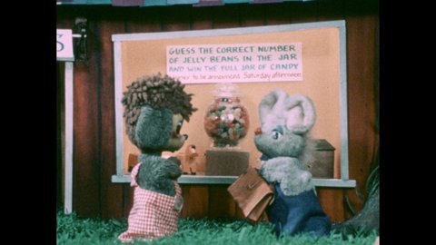 1970s: Jar of jelly beans. Animal puppets look in store window and talk. Sign says "GUESS THE CORRECT NUMBER OF JELLY BEANS IN THE JAR."