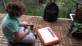 6 year old boy takes lessons , school closure due to Covid-19 Coronavirus lockdown quarantine home - lifestyle in family . Lesson magnetic board with letters on the balcony 