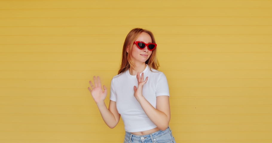 Beautiful hipster unusual woman dancing funny dance on a yellow background. Modern fashionable female in sunglasses fooling around, laughing and grimacing. Teen dancing. Royalty-Free Stock Footage #1060056659
