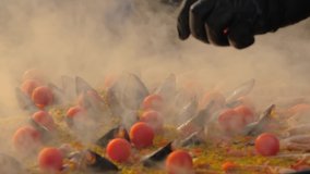 Slow motion: chef cooking paella with shrimp, mussel, rice, tomato, spice, saffron in huge paella pan at summer outdoor food market: close up. Spanish cuisine, seafood, gastronomy, street food concept - Powered by Shutterstock - Get 15% off with code: PIKWIZARD15