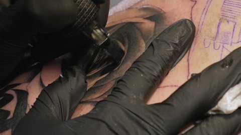 Needle tattoo machines inject a black ink into the skin of a woman. Tattoo art on body.
