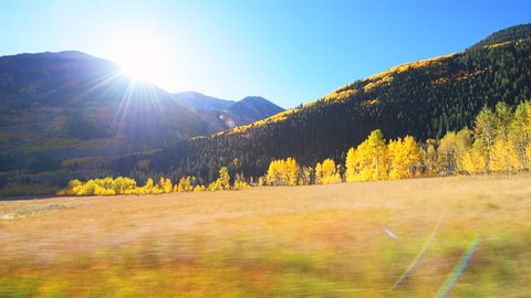 Maroon Bells car point of view side pov panning by fall golden trees in Colorado in rocky mountains and autumn yellow foliage and sun in sky