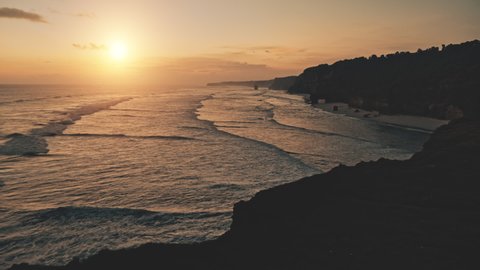Sunset at ocean bay waves slow motion aerial view. Nobody nature seascape at tropic rock shore of Sumba Island, Indonesia, Asia. Sun set light silhouette of cliff coast. Dramatic soft drone shot