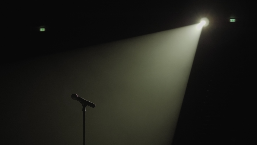 Close-up of microphone on stage against a black background with white lighting and smoke. The silhouette of the microphone in the dark. Music instrument concept. Royalty-Free Stock Footage #1060074197