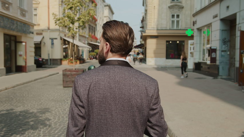 Shot back of handsome bearded man use phone walking on city street look around. Successful elegant confident man. Entrepreneur leader. Slow motion