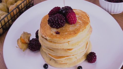 Tasty pancakes. Sweet maple syrup pouring over a stack of pancakes with fruit.