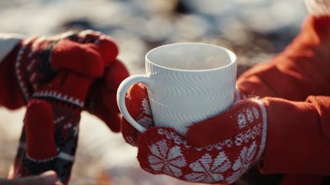 Close up hands of couple holding cups with hot tea at winter days. Coffee in the hands of a woman and a guy at xmas date. Freezing weather and warm hugs. Love concept.