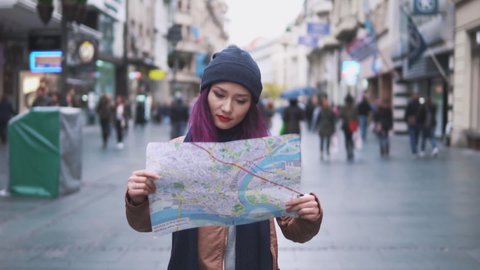Attractive young woman traveling in Europe and exploring beautiful sightseeing in Barcelona holding tourist map on hands, enjoying holiday time. Pretty tourist woman examining the map of the city.