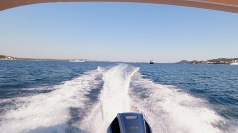 Boat with canopy and outboard motor makes large wake on blue Adriatic