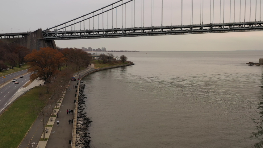On a cloudy day the drone camera dollys in beside Shore Parkway. The Verrazzano-Narrows Bridge is in the background. The drone flies over the Hudson River in Brooklyn, NY | Shutterstock HD Video #1060086560
