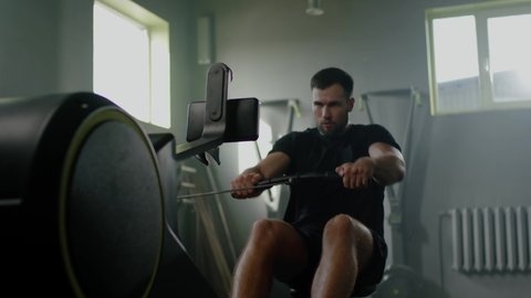 Sportsman Do Hard Exercises With Rowing Machine .