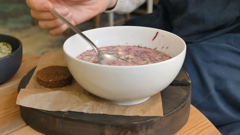 Young brunette in coloured pullover eats raw food vegetarian soup from bowl with spoon in vegan restaurant slow motion closeup