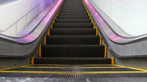 Low angle looped perspective view of modern escalator stairs. Automated elevator mechanism. Yellow line on stairway illuminated with purple light. Futuristic empty machinery staircase moving straight.