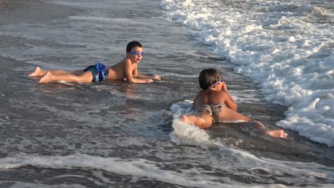 Calis beach, Fethiye, Turkey - 19th of September 2020: 4K Two boys play and tumble rolling in the beating sea waves
