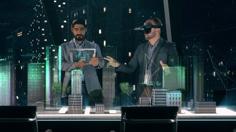 In the Near Future: Professional Designer in Suit wearing AR Headset presenting Architecture Project to Partner standing around Futuristic Table with Holographic Modern Augmented Reality Technology.